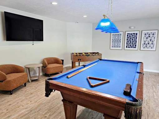 A pool table is in the middle of a room with a blue light hanging from the ceiling.