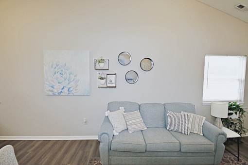 A living room with a grey couch and a painting on the wall.