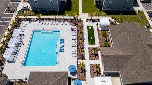 An aerial view of a swimming pool surrounded by a grassy area and a parking lot.