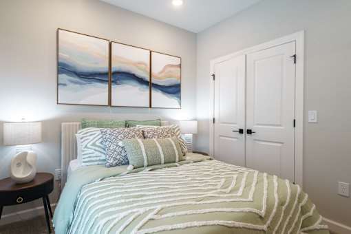 A bedroom with a bed, a nightstand, and a painting on the wall.