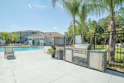 Grill with a palm tree and pool in the background at Trillium apartments in Melbourne fl