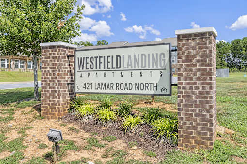 A sign for Westfield Landing Apartments stands in front of a brick building.