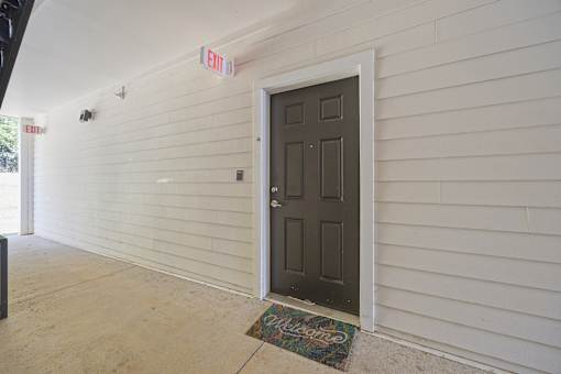 A white building with a brown door and a green mat on the floor.