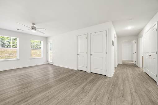 A room with white walls and wooden flooring with a ceiling fan.