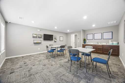 A room with a grey carpet and a white table with blue chairs.