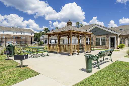 A gazebo is surrounded by benches and trash cans in a park.