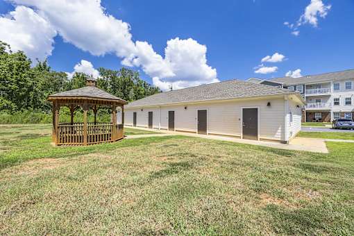 A gazebo sits in a grassy field next to a building.