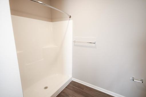 A white shower stall in a bathroom with a wooden floor.