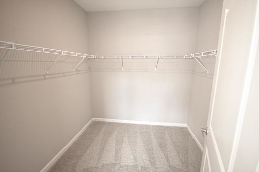 A white closet with a carpeted floor and a metal rack.