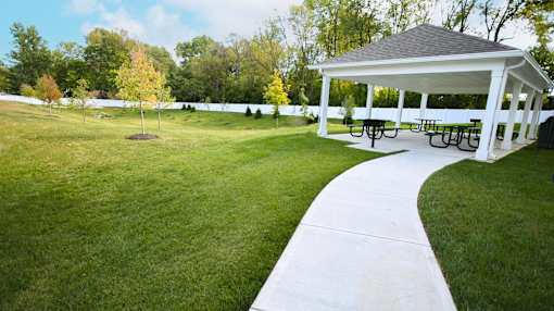 A pavement pathway leads to a pavilion with picnic tables.