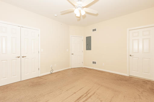 a empty bedroom with a ceiling fan and two doors