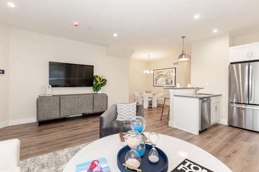 A modern living room with a grey sofa, a white coffee table, and a kitchen in the background.