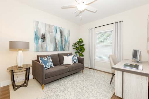 A living room with a grey couch, a table with a lamp and a painting on the wall.