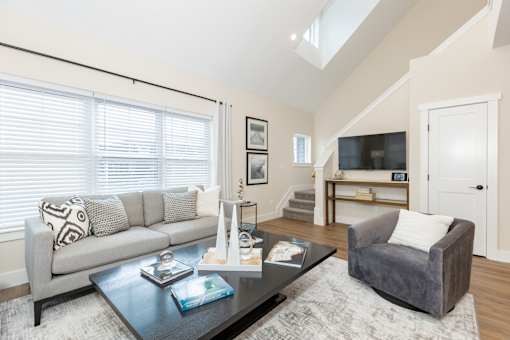 A living room with a grey couch, a grey armchair, a coffee table, and a staircase in the background.