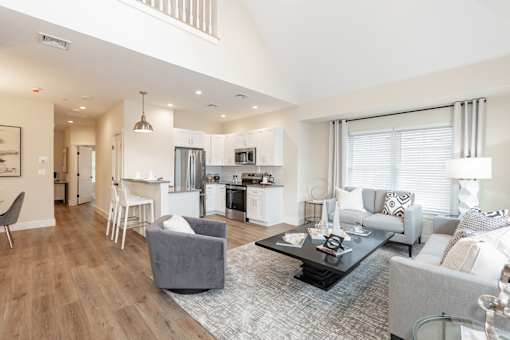 A modern living room with a grey sofa, a grey armchair, a black coffee table, and a kitchen in the background.