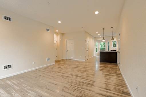 an empty living room and kitchen with wood floors and white walls