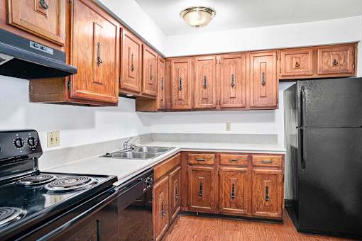 A kitchen with wooden cabinets and black appliances at Hampton in Highland Apartments, Indiana, 46322
