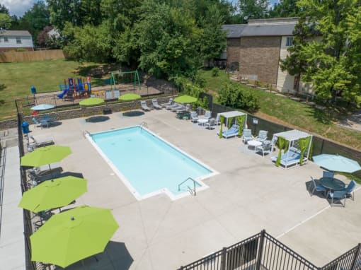 a swimming pool with lounge chairs and umbrellas in front of a brick building at Stonewater Apartments, Louisville, KY 40241