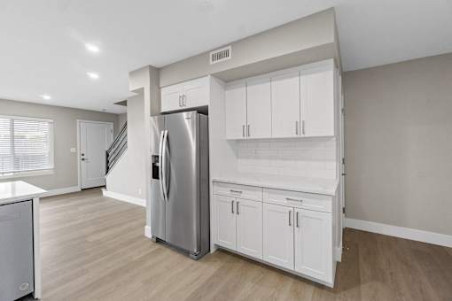 A kitchen with a refrigerator, cabinets, and a staircase.