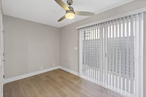A room with a ceiling fan and a sliding door with blinds.