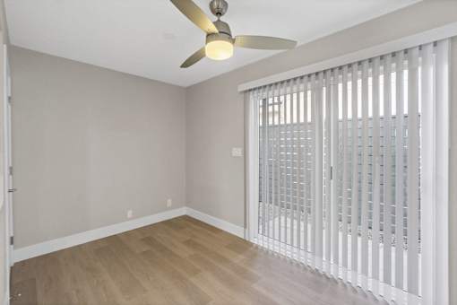 A room with a ceiling fan and a sliding door with blinds.