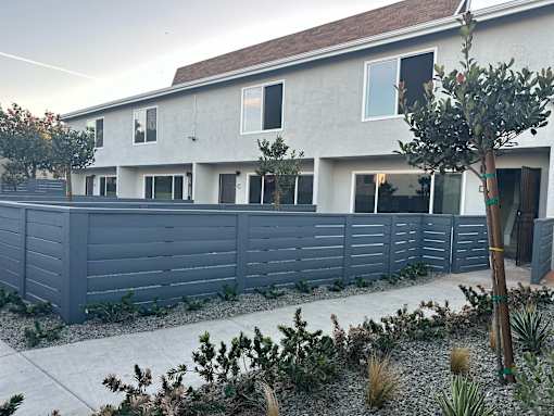 A grey house with a grey fence and a green tree in front.