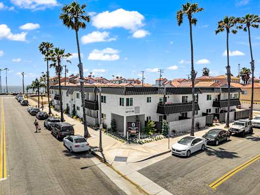 A row of white buildings with palm trees in front.