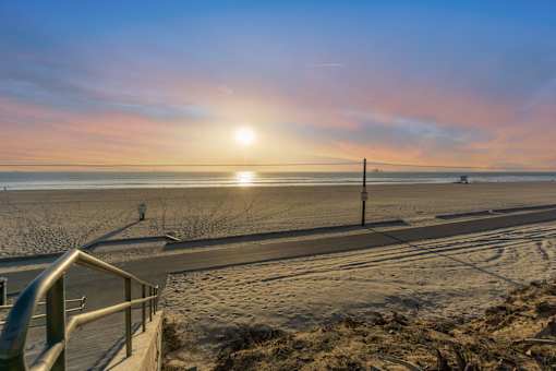 A sunset view of a beach with a metal railing in the foreground at Ocean Breeze Terrace Apartment, Huntington Beach