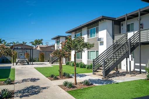 A sunny day at a modern apartment complex with a well-maintained lawn and a staircase leading to the entrance.
