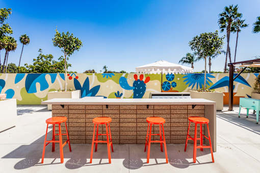 A bar with orange stools in front of a wall with a mural. at The Reserve La Mirada, California, 90638