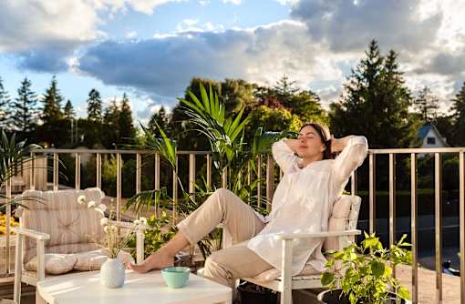 A person is sitting on a chair with their hands behind their head on a balcony.