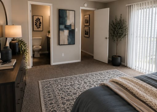 A bedroom with a bed, a nightstand, a lamp, a rug, a plant, and pictures on the wall.