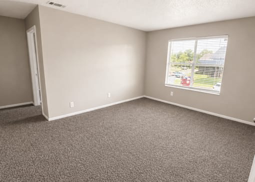 A room with a carpeted floor and a window showing a parking lot outside.