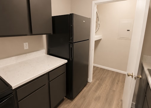 A black refrigerator in a kitchen with brown cabinets.