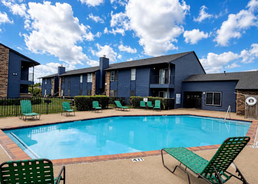 A swimming pool surrounded by green chairs and a building in the background.
