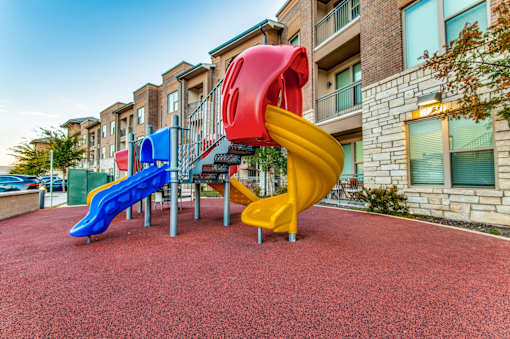 A playground with a red slide and a yellow slide in front of a building.