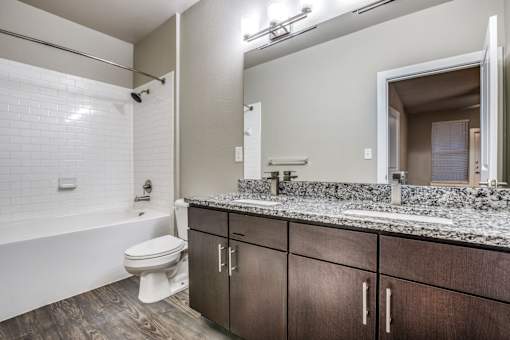 A white toilet sits in a bathroom with a wooden floor and a white bathtub.