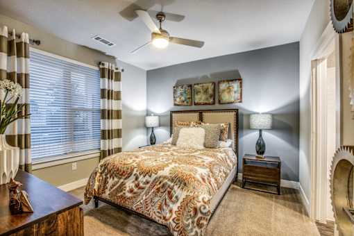 A bedroom with a patterned bedspread and a ceiling fan.