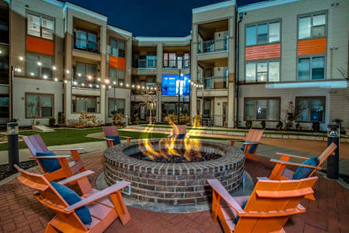A fire pit in the middle of a patio surrounded by orange chairs.