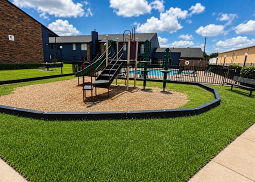 A playground with a slide and sandbox in front of a building.