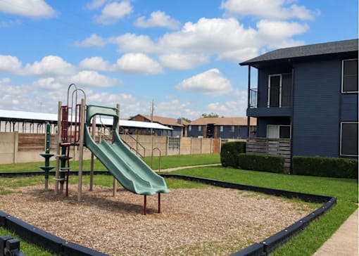 A playground with a green slide and a blue building in the background.
