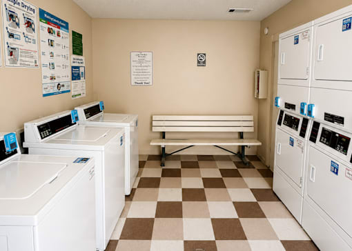 A laundromat with washers and dryers and a bench.
