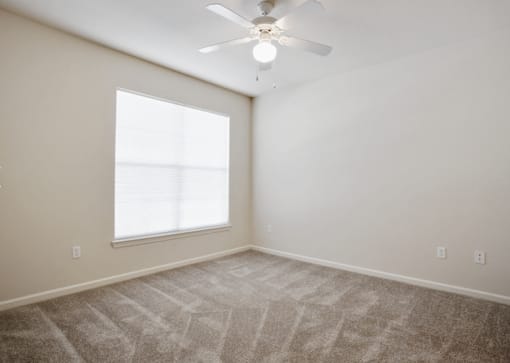A room with a ceiling fan and a large window at Addison Park Apartments in Arlington, TX.