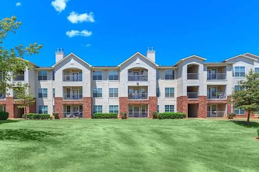 A large apartment complex with a green lawn in front at Addison Park Apartments in Arlington, TX.