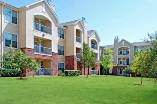 Apartment complex with green grass in front at Addison Park Apartments in Arlington, TX.