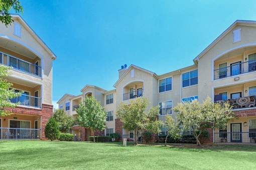 Apartment complex with green lawn and trees at Addison Park Apartments in Arlington, TX.