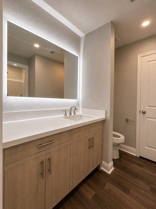 A bathroom with a white counter top and wooden cabinets.