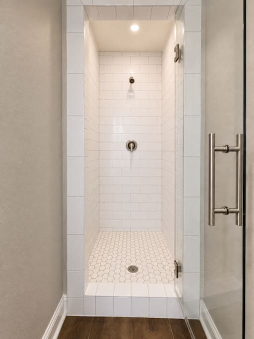 A white tiled shower with a drain in the middle.