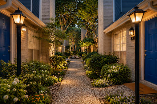A cobblestone pathway leads between two houses with lit up lamps on either side.
