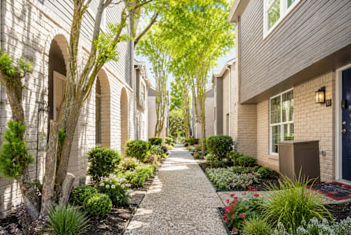 A pathway leads through a row of houses with trees on either side.